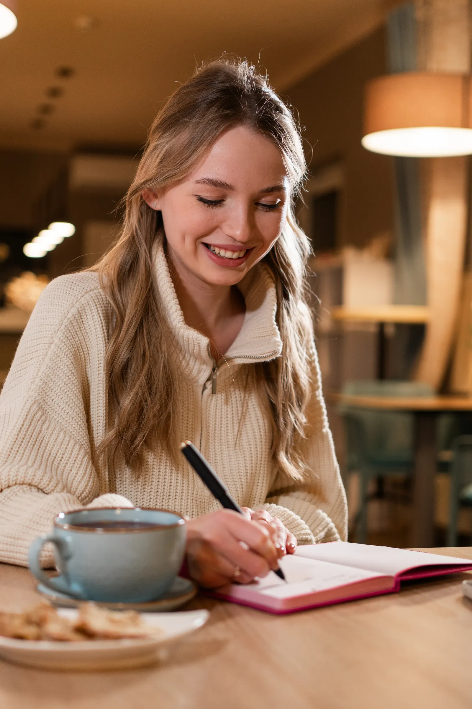 A woman writing in a planner over a cup of coffee.